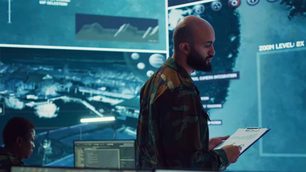 A military officer reviews a report in a high-tech operations room.